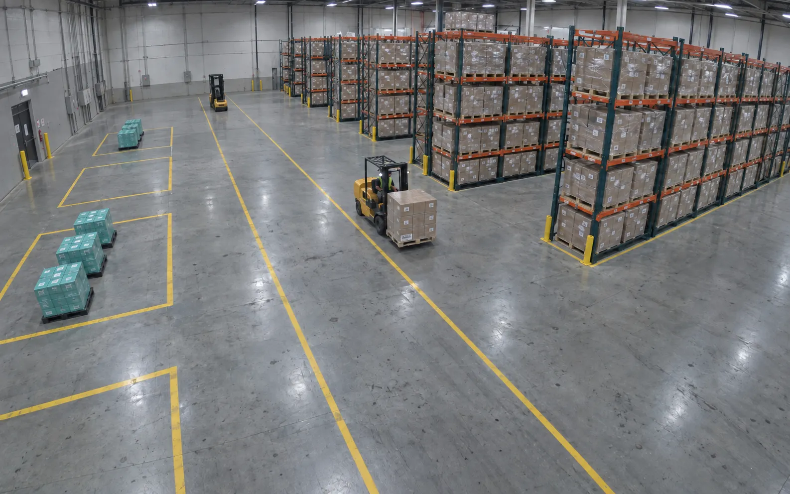 Ceiling camera view of a forklift carrying a pallet between storage and staging.